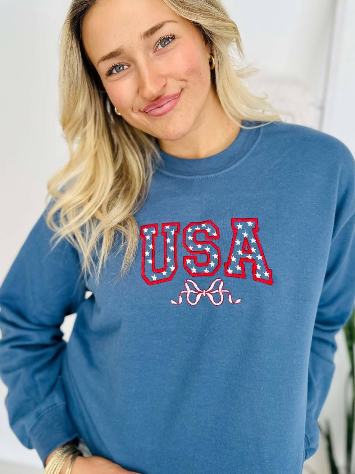 A woman wearing a blue sweatshirt with 'USA' and a star and bow embroidered on the front.