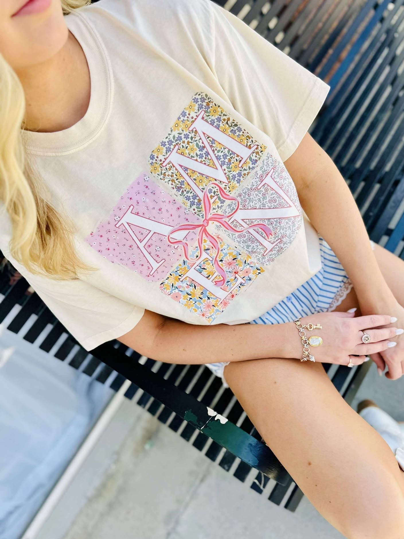 Person wearing a white t-shirt with colorful AMEN letter design sitting on a bench.