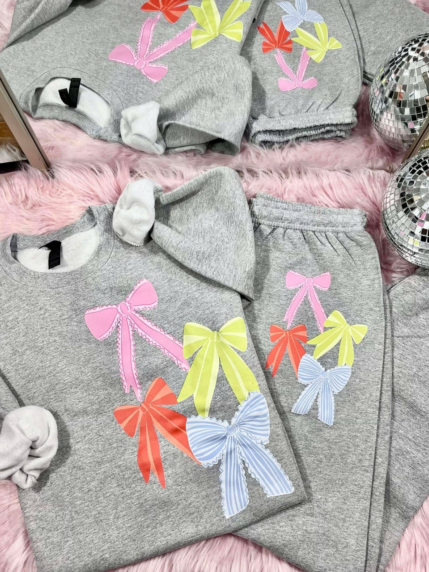 Gray sweatshirt and pants set with colorful bows on a pink surface.