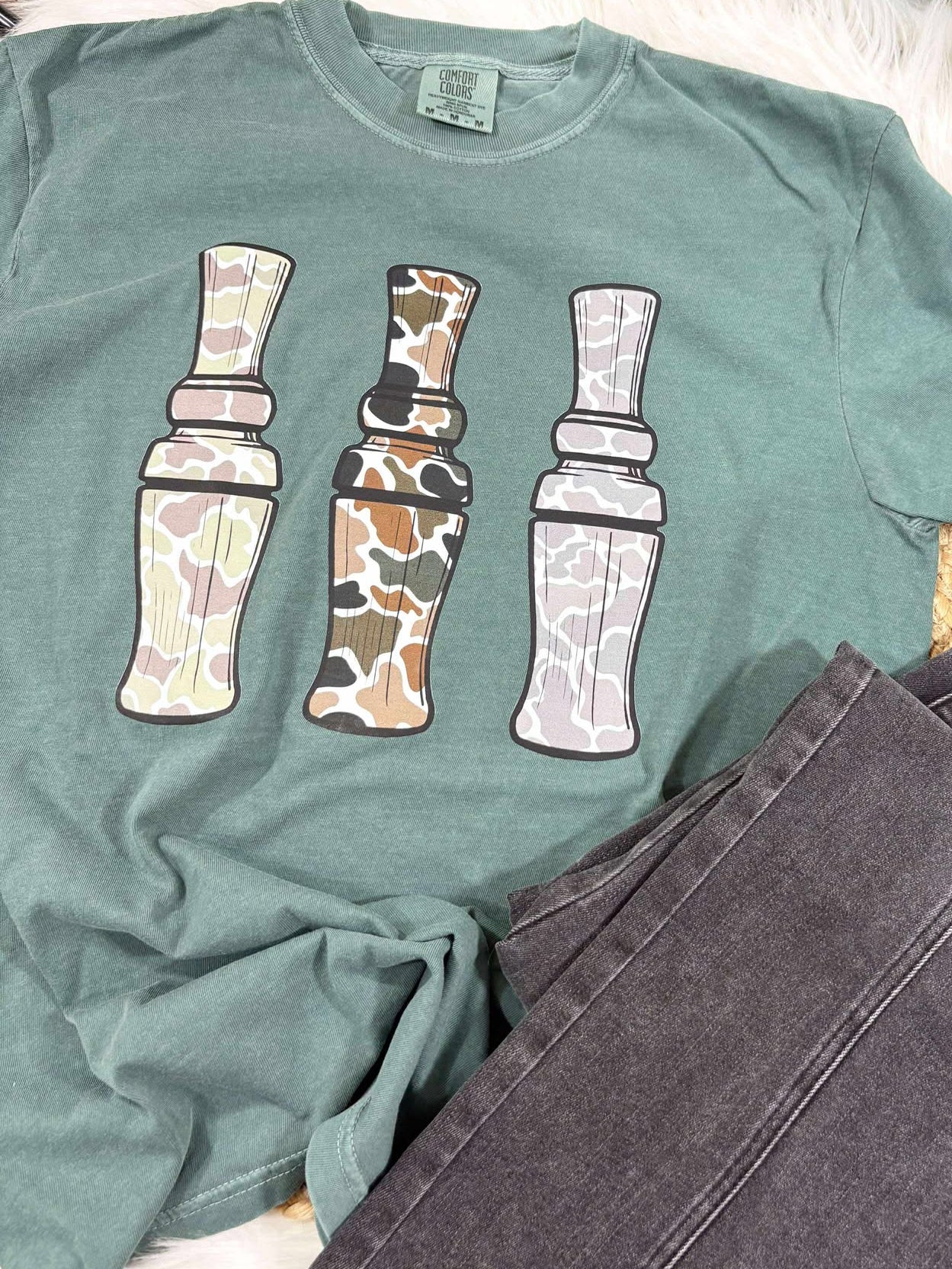 Green t-shirt with three camouflaged duck call designs on a white surface.