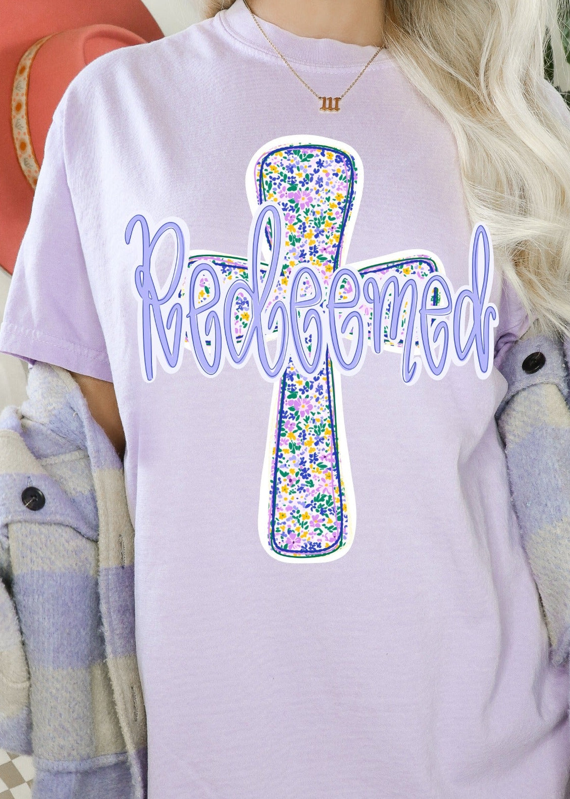 Person wearing a light purple t-shirt with a floral cross design and 'Redeemed' text.