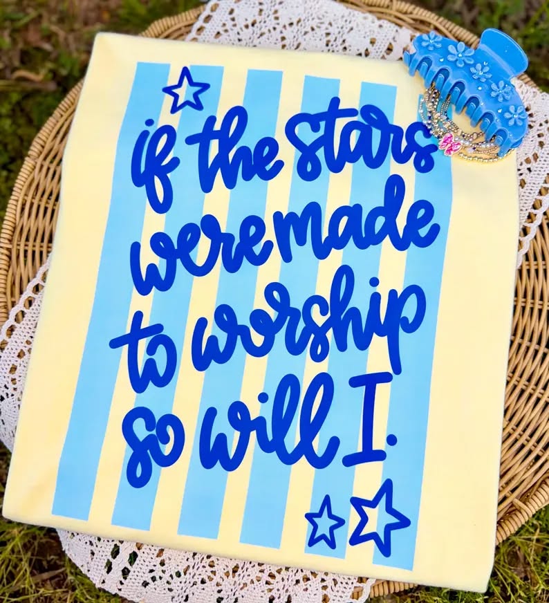 Wooden sign with blue text and stars on a yellow background, placed on a woven surface.