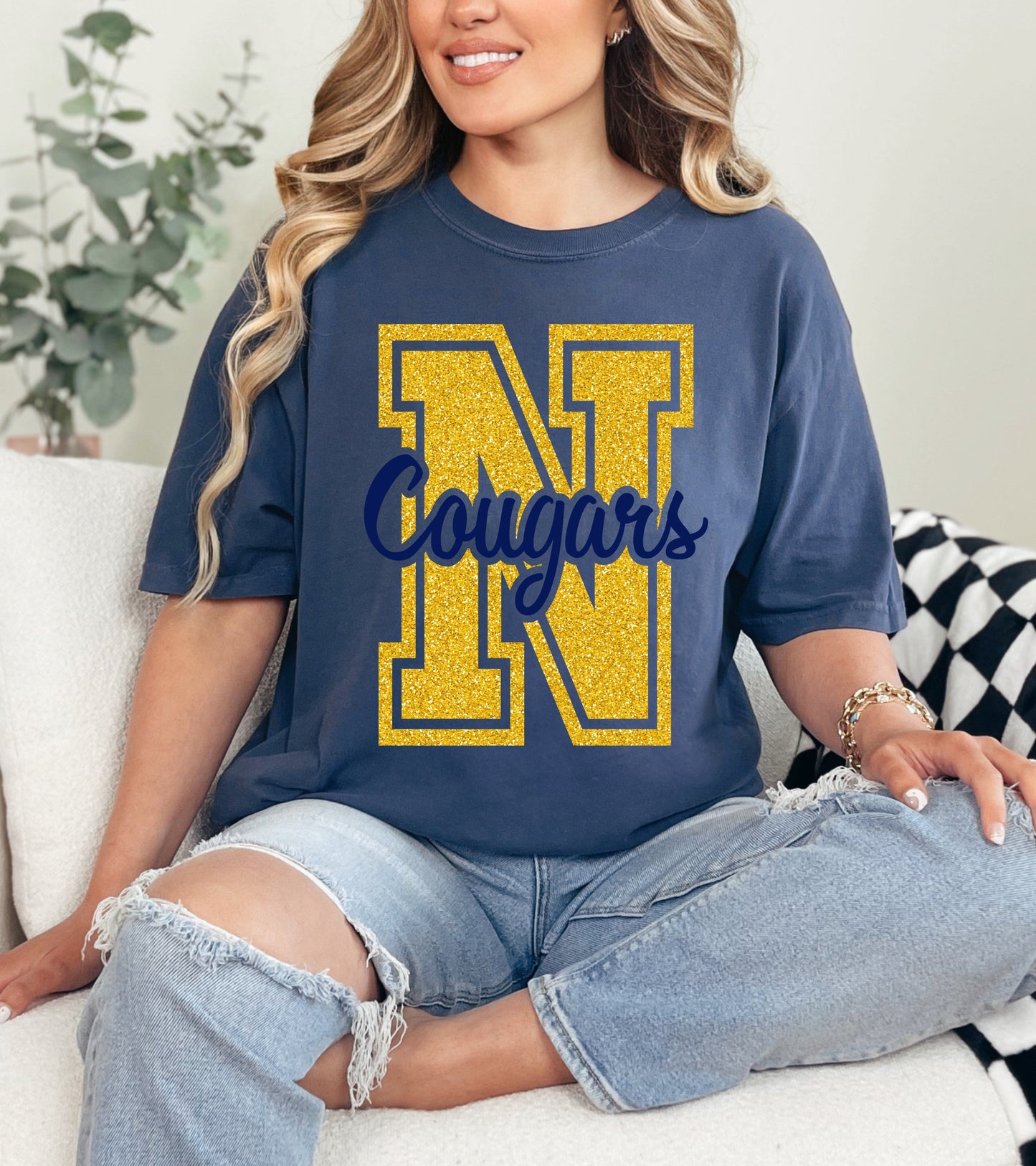 Woman wearing a blue t-shirt with 'N Cougars' design, sitting on a couch.