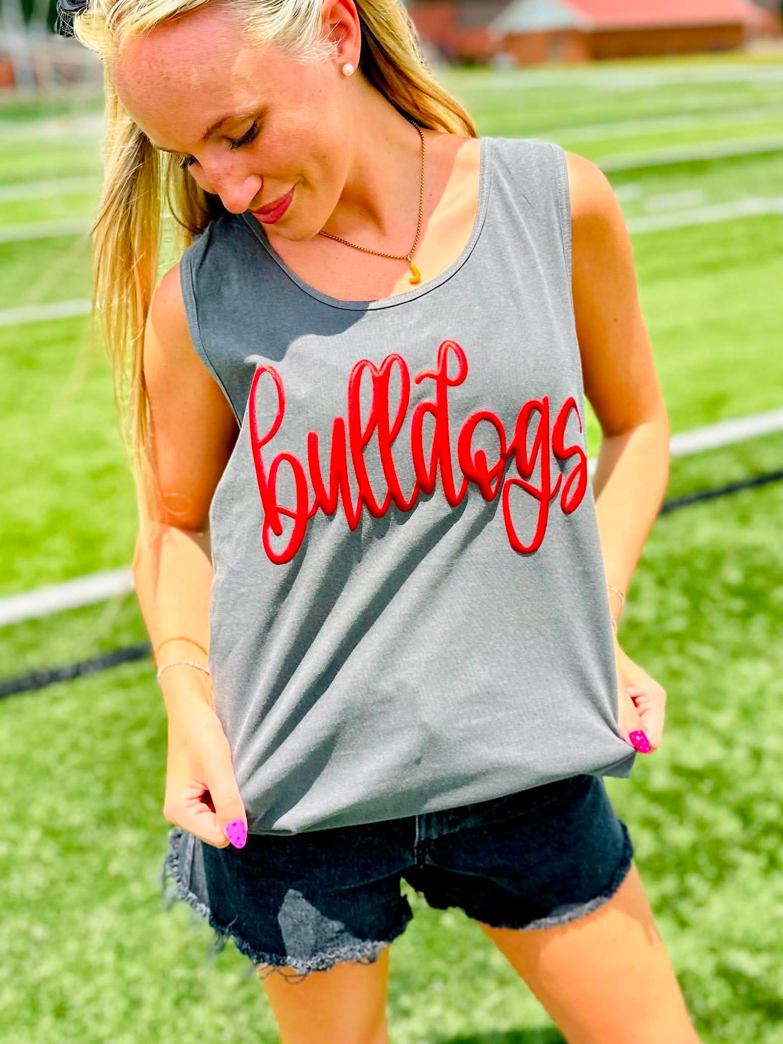 Woman wearing a gray tank top with 'Bulldogs' in red text on a grassy field.