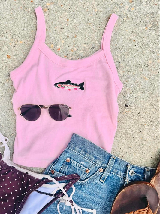 Pink tank top with Rainbow trout, sunglasses graphic, blue jeans, and brown sandals on a beach surface