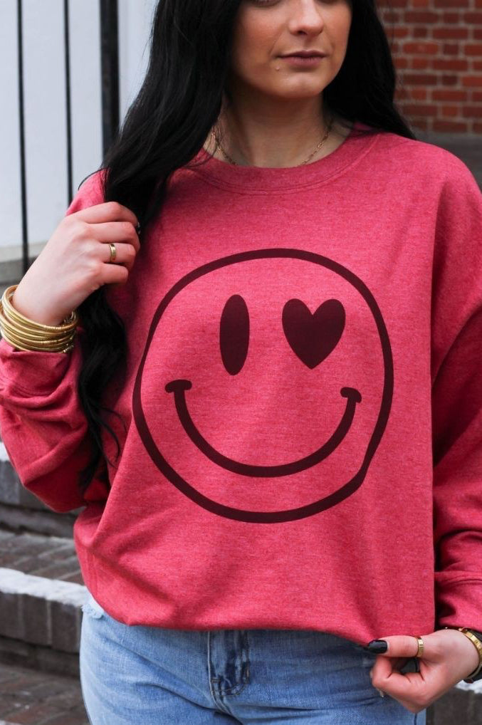 Person wearing a red sweatshirt with a smiley face design outdoors.