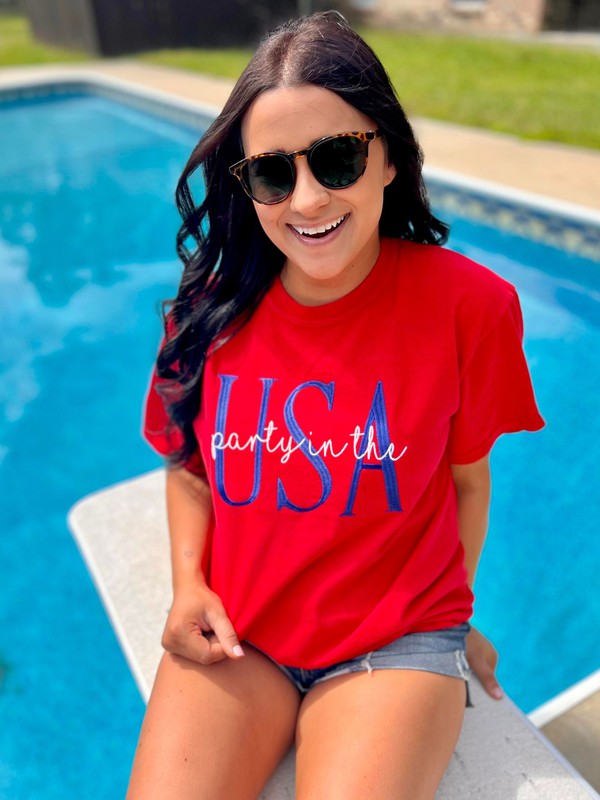 A person wearing a red t-shirt with the text 'PARTY' and 'USA' embroidered on it, sitting by a pool.