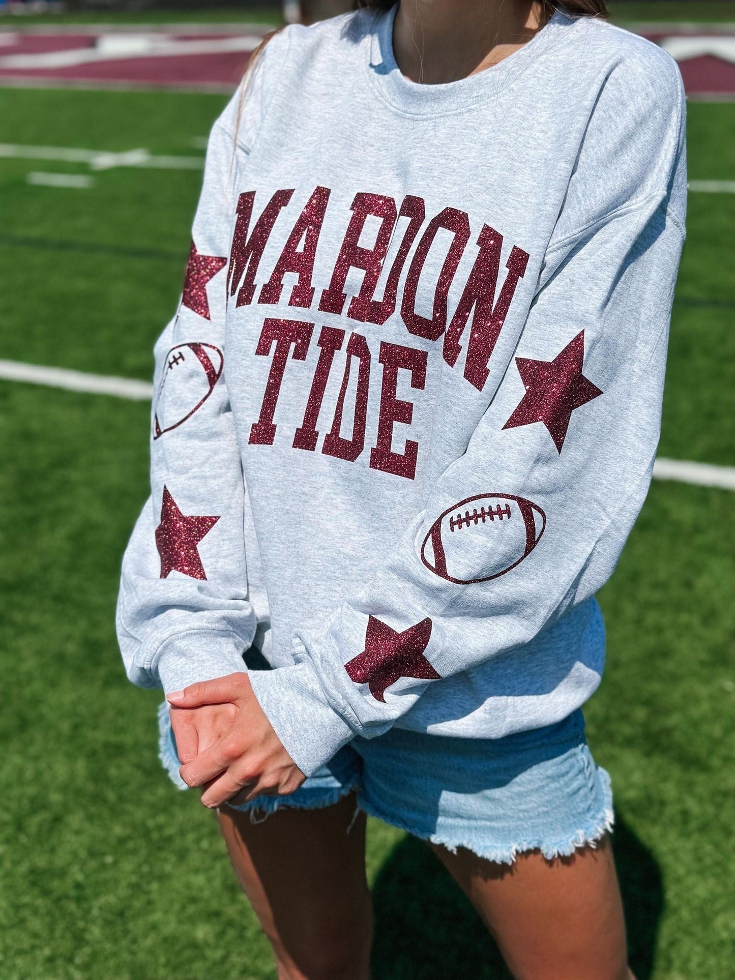 Person wearing a gray sweatshirt with 'Marion Tide' text and sports graphics on a grassy field.