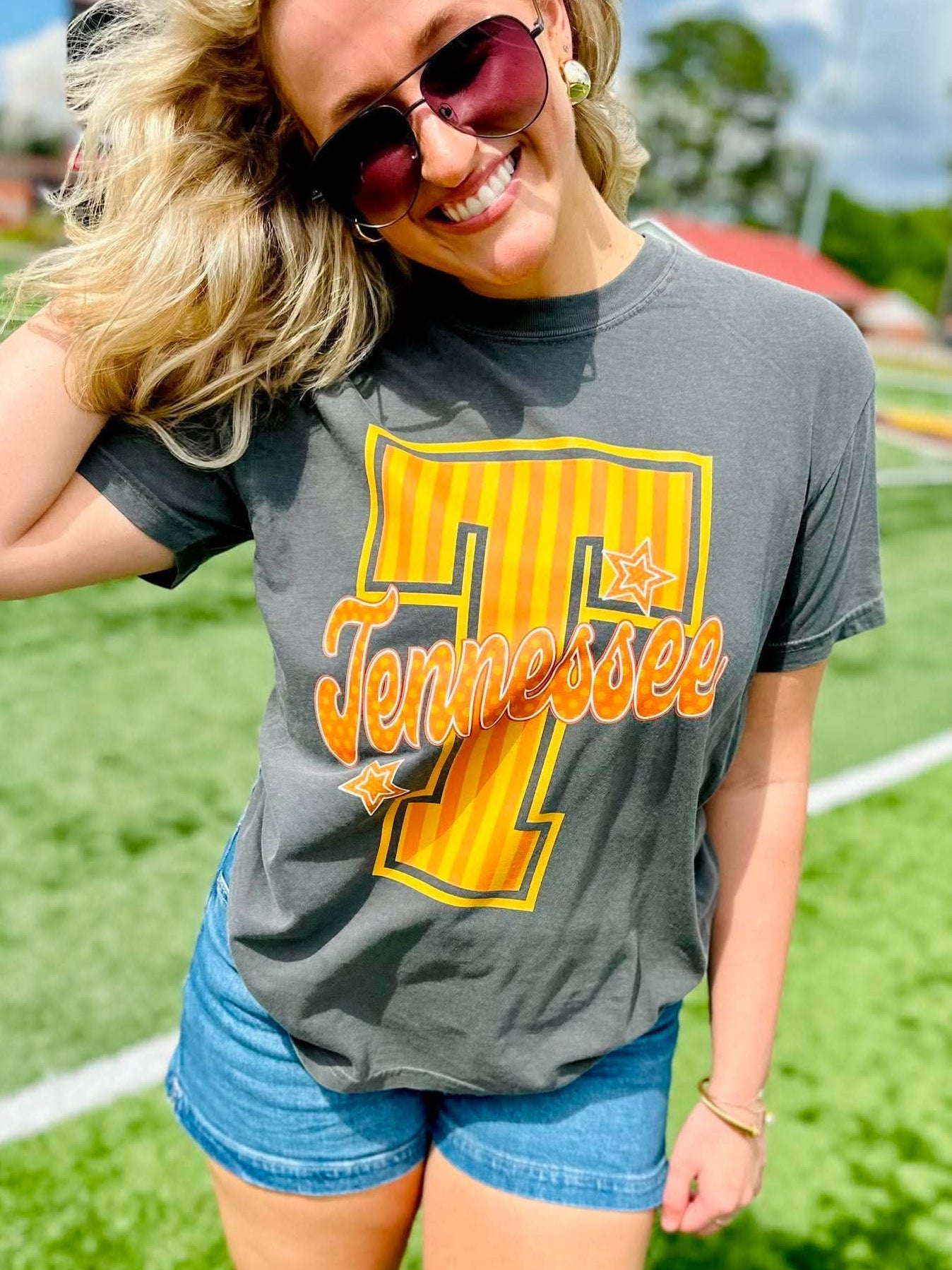 Woman wearing a gray t-shirt with a large yellow number '1' and 'Tennessee' text, standing on a grassy field.