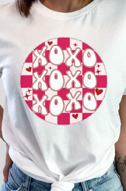 A person wearing a white t-shirt with a red and pink checkered pattern on it, and the text 'XOXO' in the center.