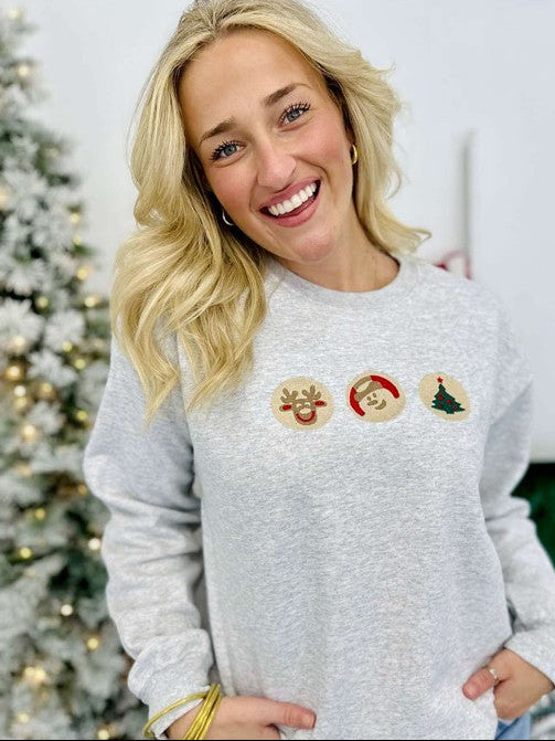 Person wearing a Ash sweatshirt with Christmas-themed cookies in front of a decorated Christmas tree.
