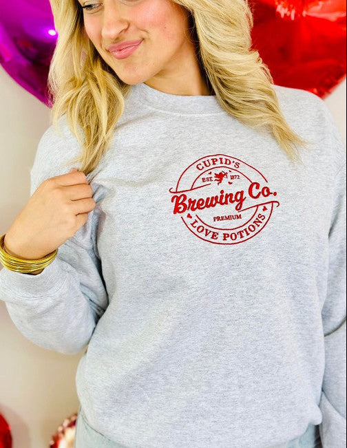Person wearing a gray sweatshirt with 'Cupid Brewing Co.' logo, surrounded by heart-shaped balloons.