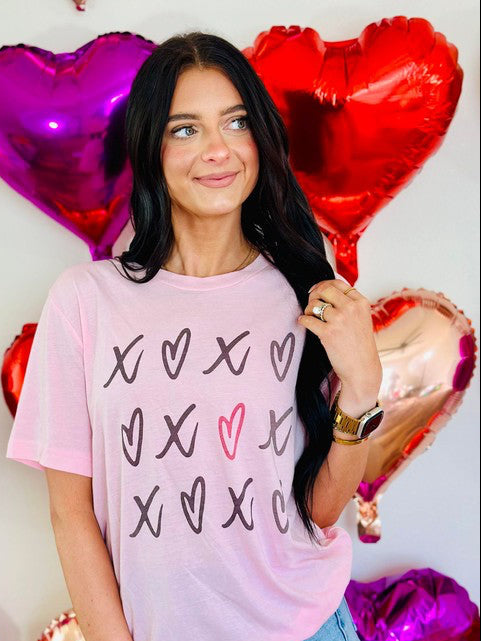 A person wearing a pink t-shirt with heart and 'XOXO' text design, surrounded by balloons and decorations with a Valentine's Day theme.