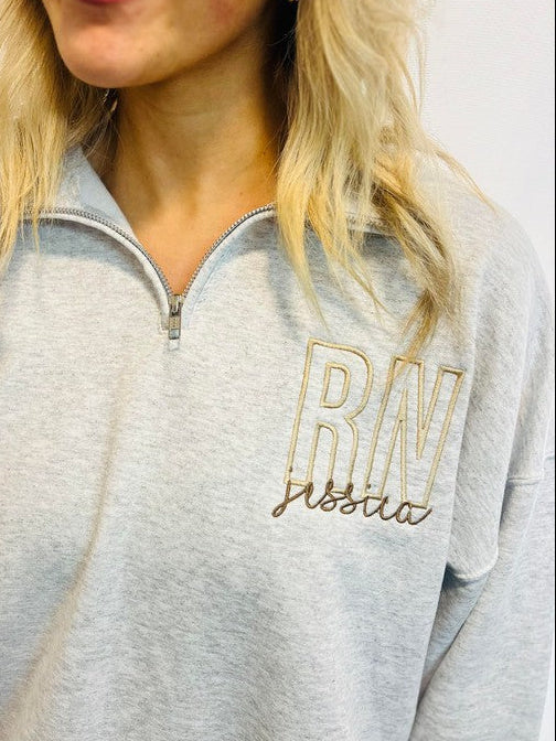 A woman wearing a gray sweatshirt with 'RN' embroidered on the front.