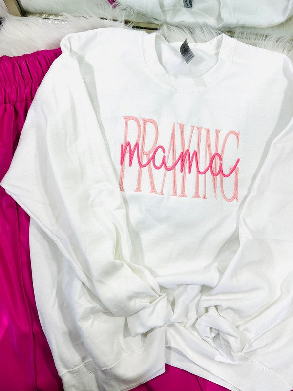 White embroidered sweatshirt with the text 'PRAYING Mama' and a graphic of a mother holding a child.