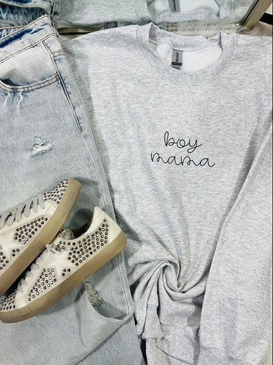 A gray sweatshirt with the text 'BOY MAMA' embroidered on the front, paired with blue jeans and white sneakers with embellishments on the sole.