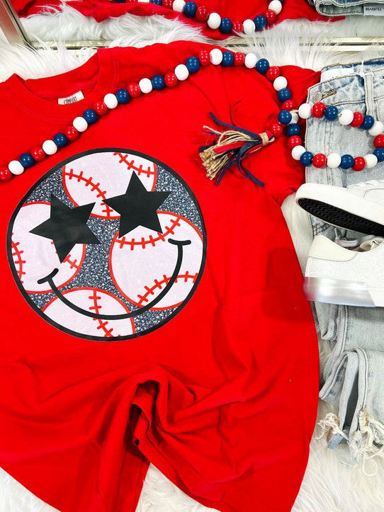 A red graphic tee with a baseball and stars design, accompanied by blue and white beaded necklaces and a black hair tie.
