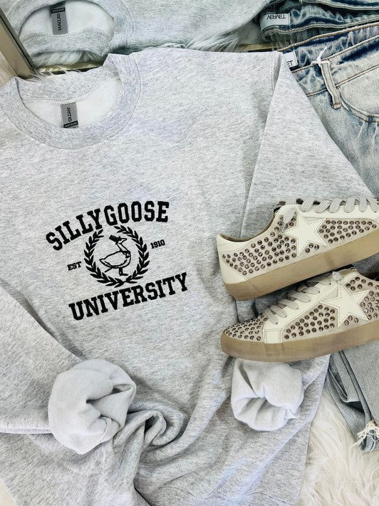A gray embroidered sweatshirt with 'Silly Goose University' text on the front, paired with white sneakers with embellishments on the sole.