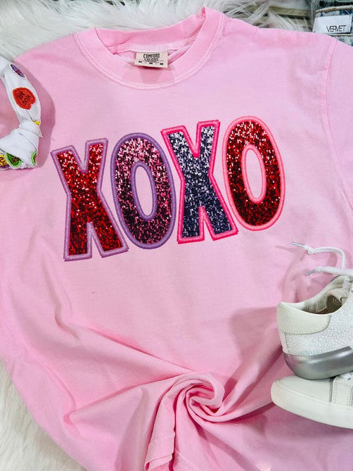 Pink sweatshirt with 'XOXO' in colorful letters on a white surface.