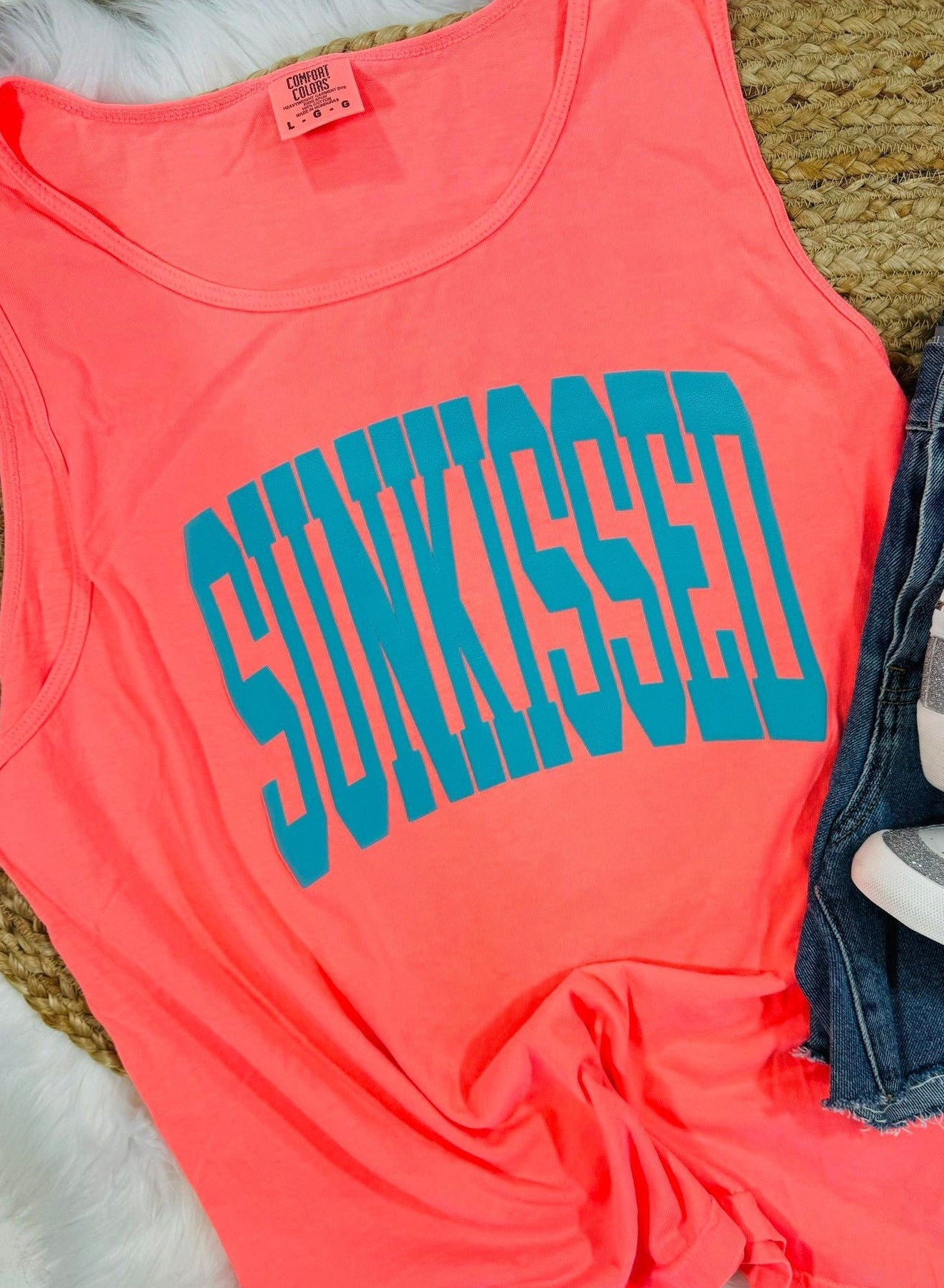Coral tank top with 'SUNKISSED' text on a textured surface