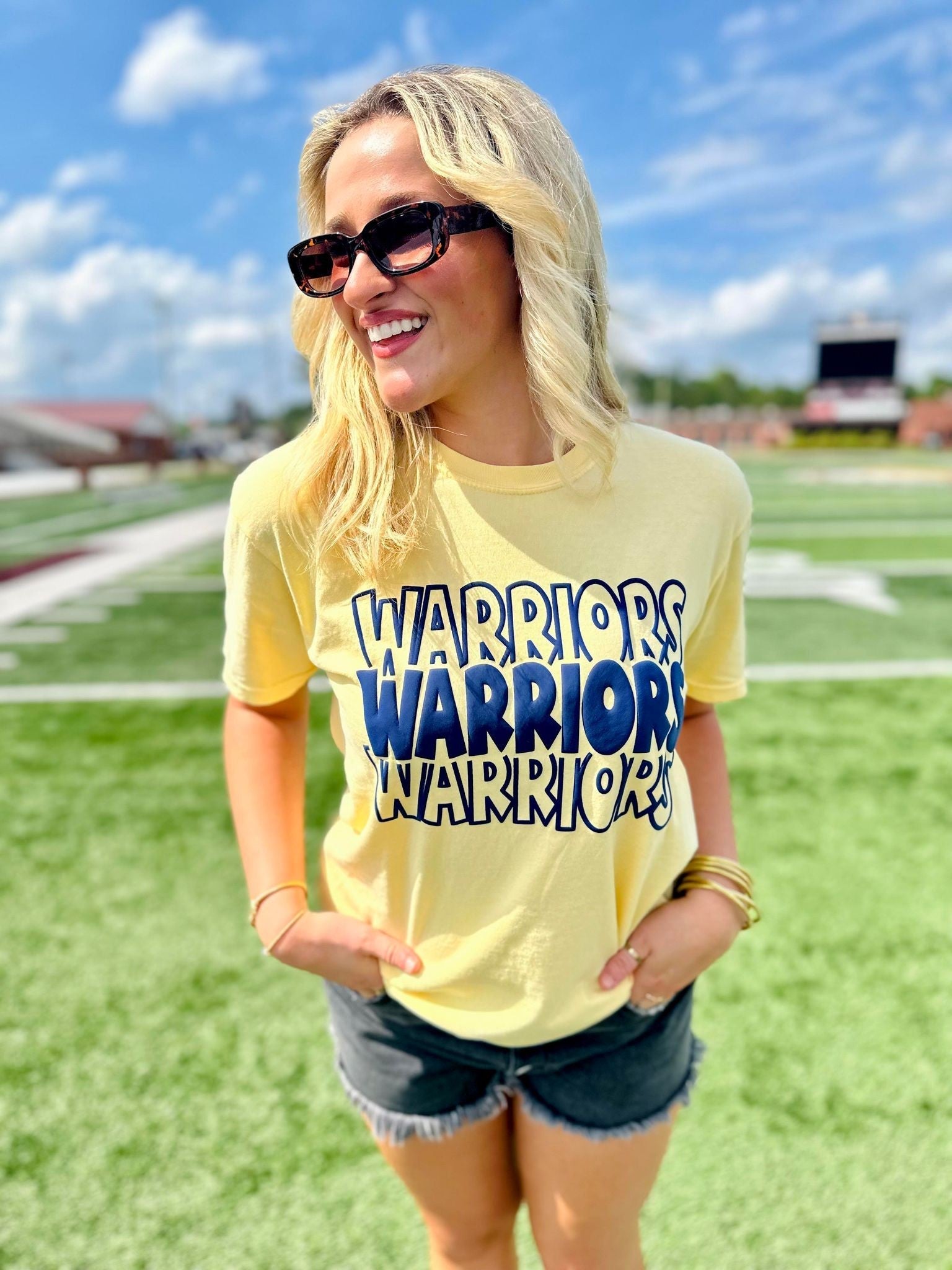 Woman wearing a yellow t-shirt with 'Warriors' text on a sports field