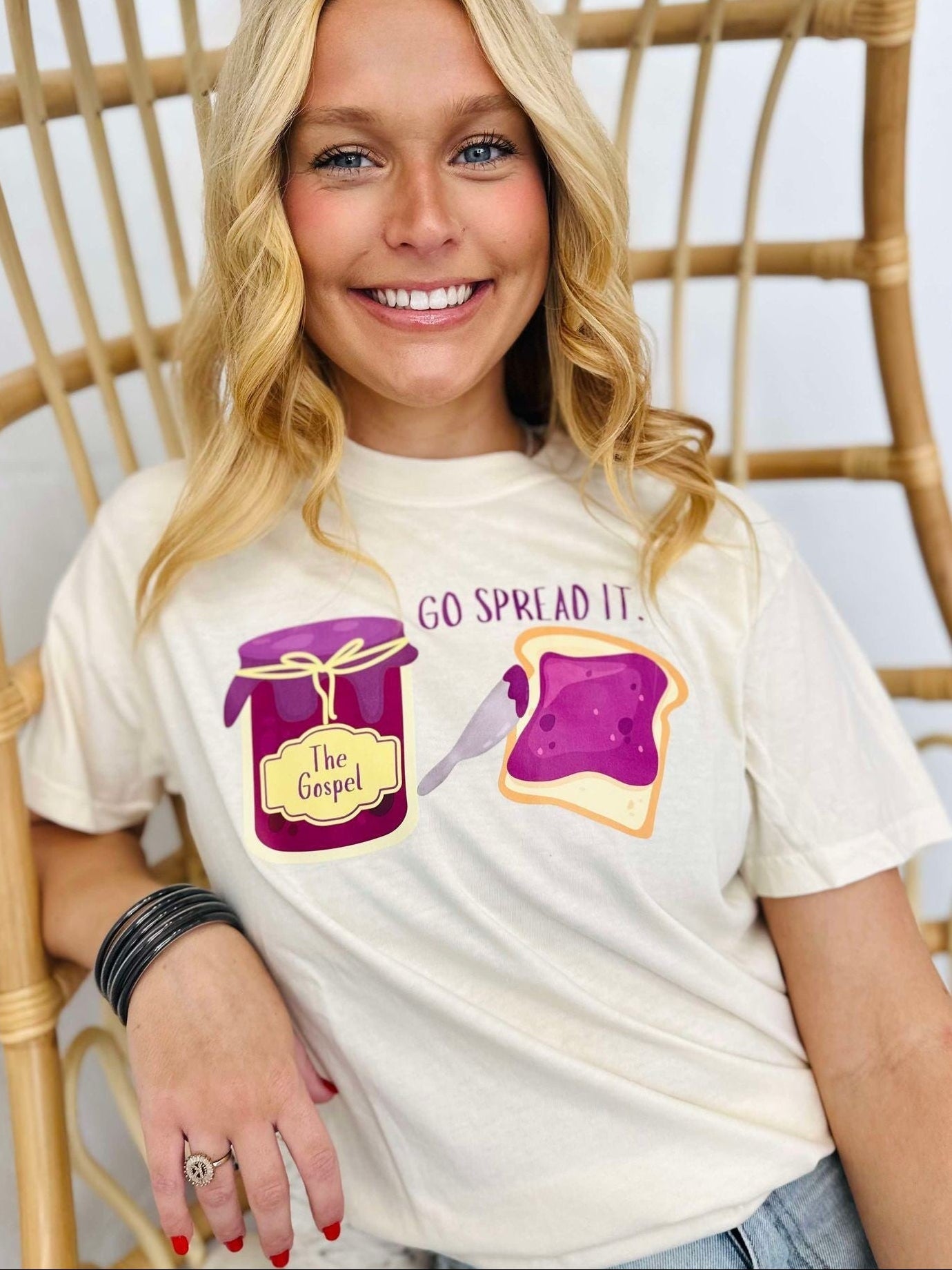 Person wearing a white t-shirt with graphics and text "Go spread it", sitting on a wicker chair.
