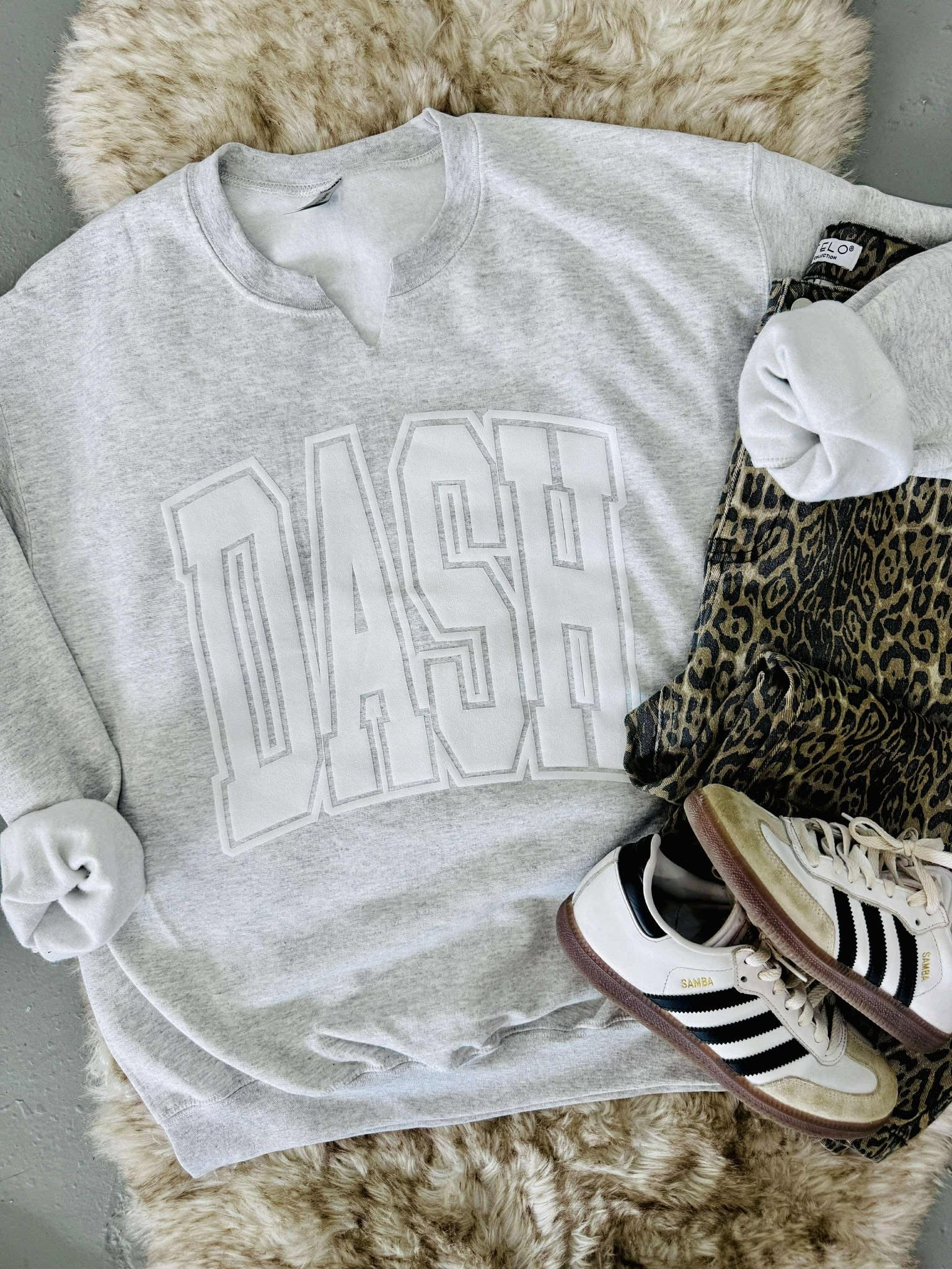 Gray sweatshirt with 'DASH' text, Adidas sneakers, and leopard print item on a fur surface
