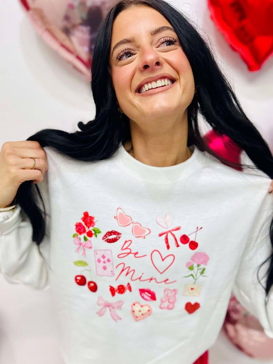 Woman wearing a white sweatshirt with Valentine's Day designs surrounded by heart-shaped decorations.