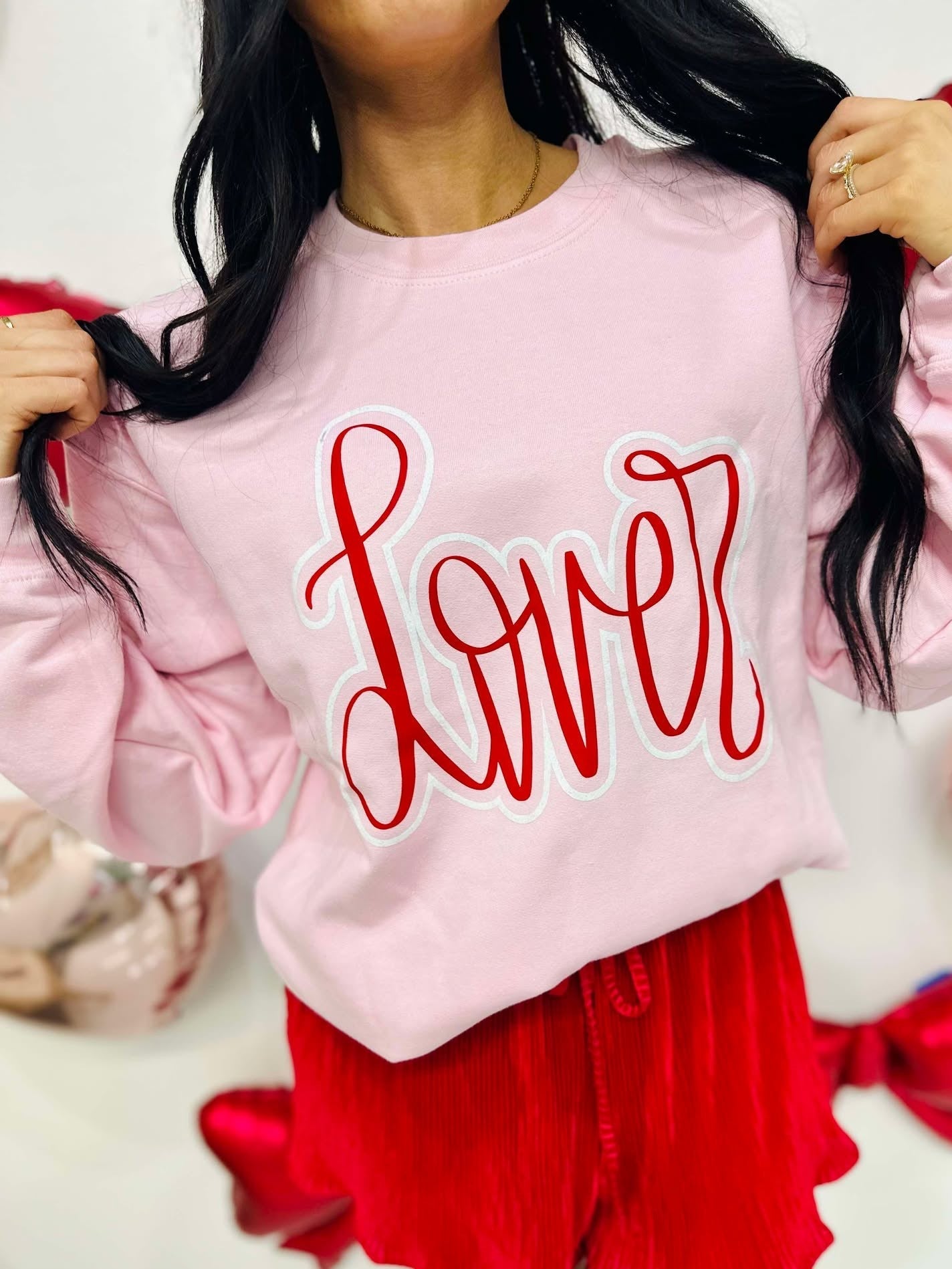 Person wearing a pink sweatshirt with 'Lover' written in red, standing against a white background.