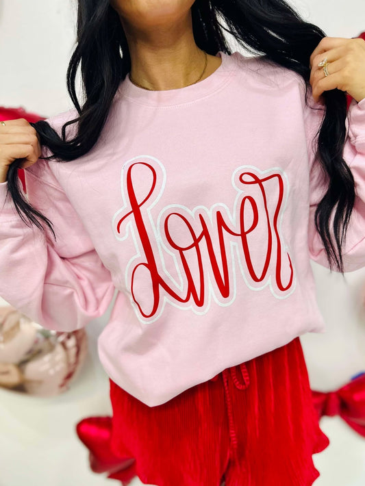 Person wearing a pink sweatshirt with 'Lover' written in red, standing against a white background.