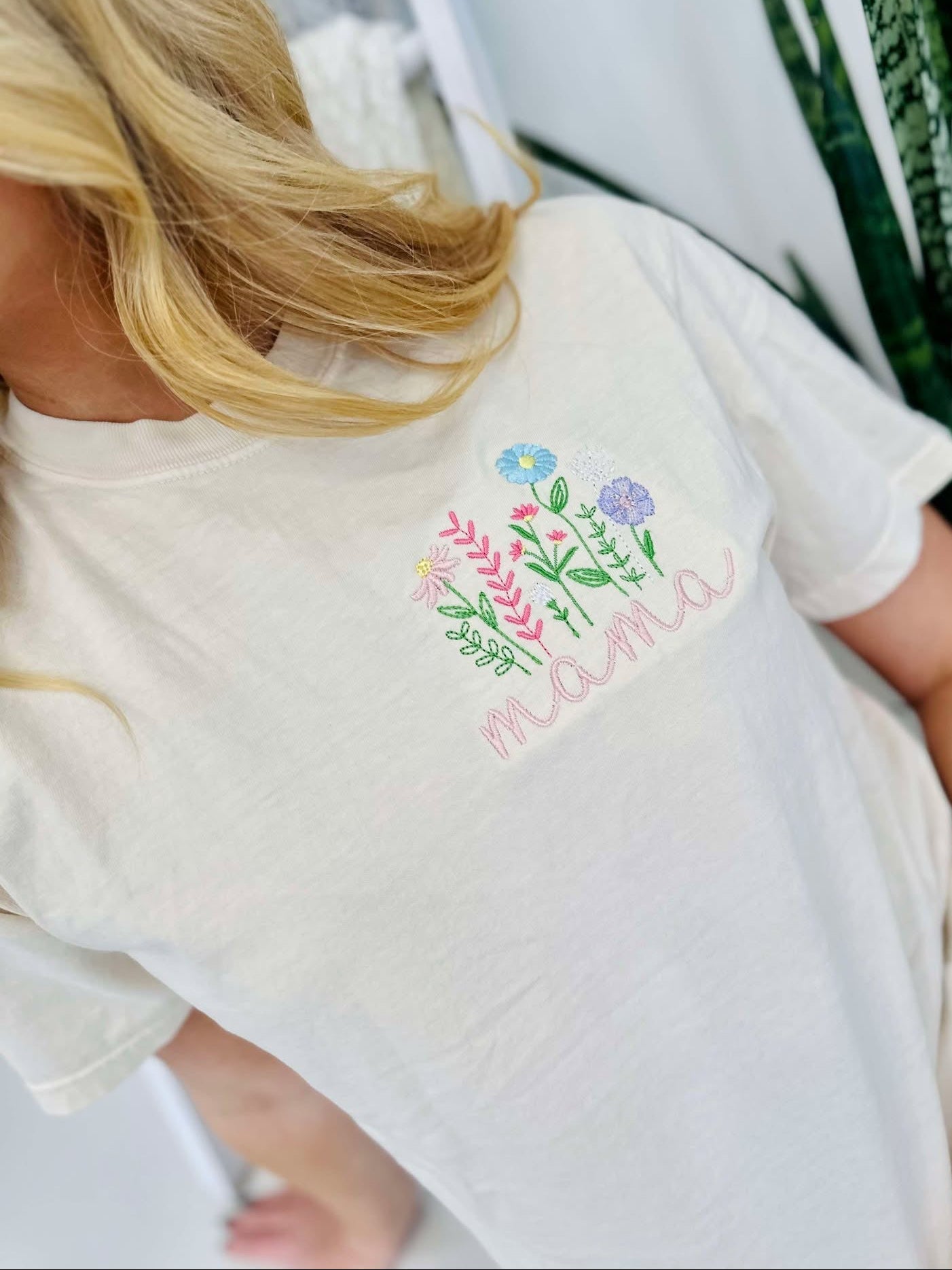 A woman wearing a white short-sleeved t-shirt with embroidered floral design and the word 'mama' on the front.