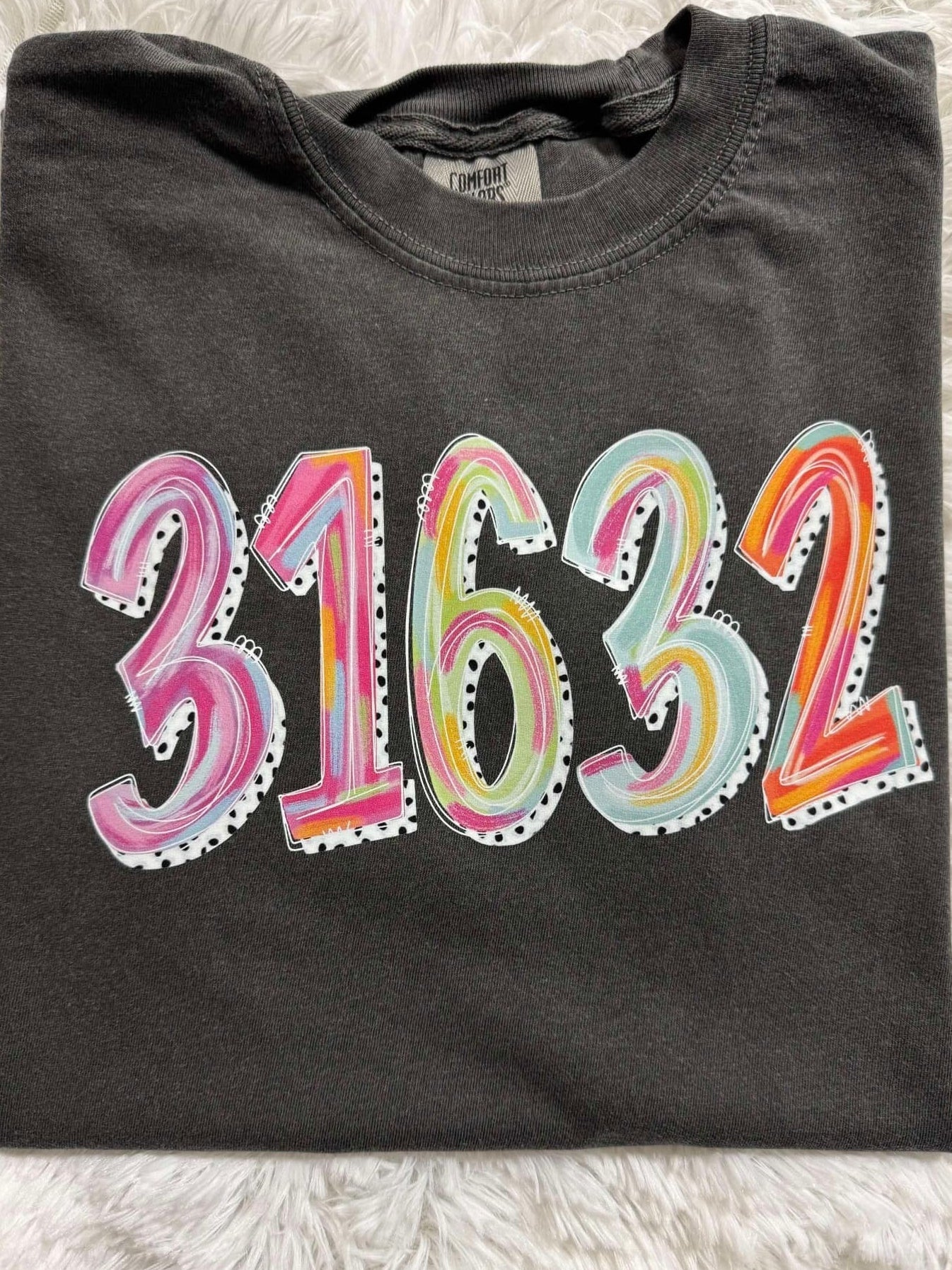 A folded black t-shirt with the zip code '31632' painted in various colors on the front.