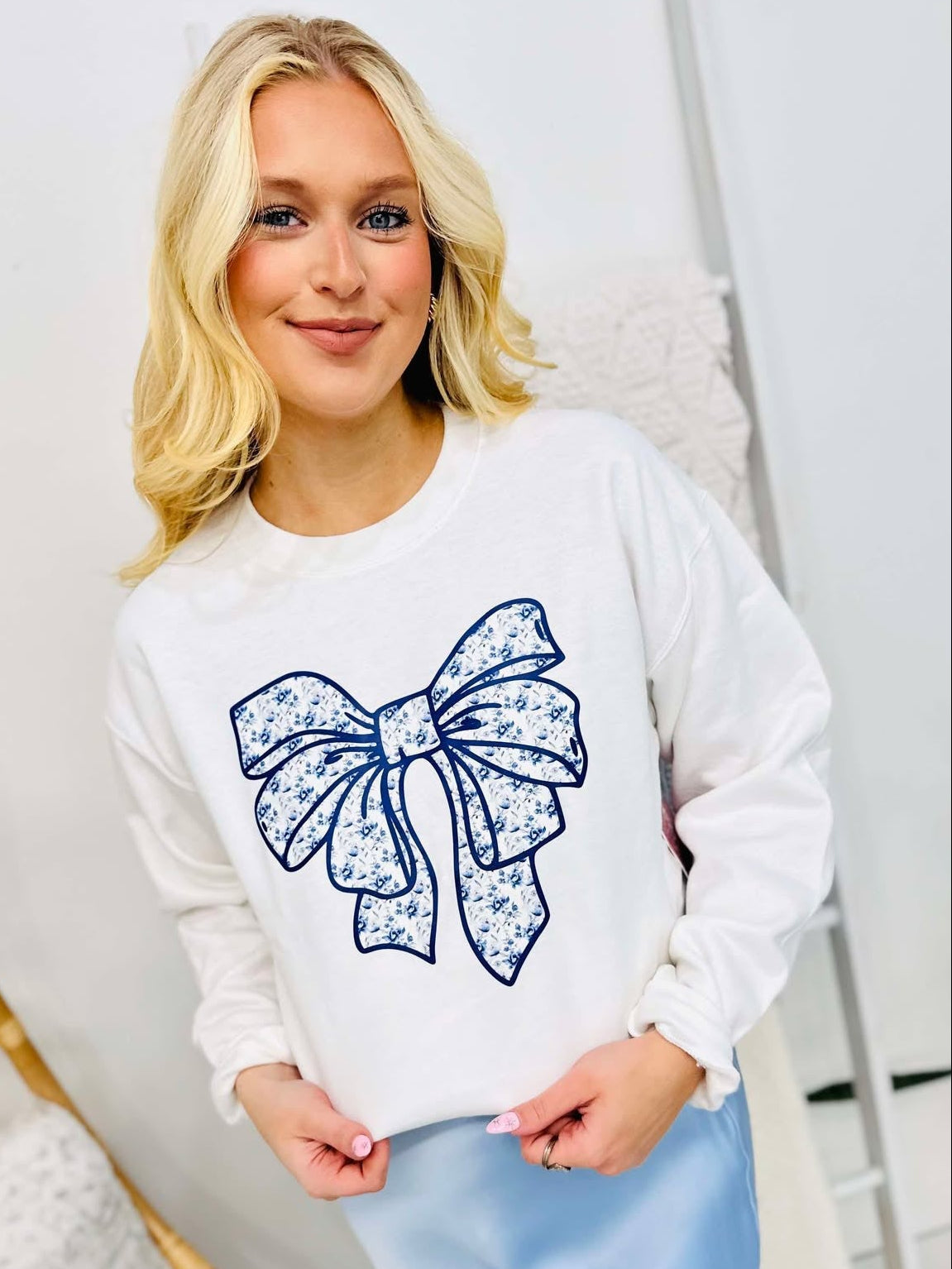 A woman wearing a white sweatshirt with a blue Chino bow graphic design on the front.