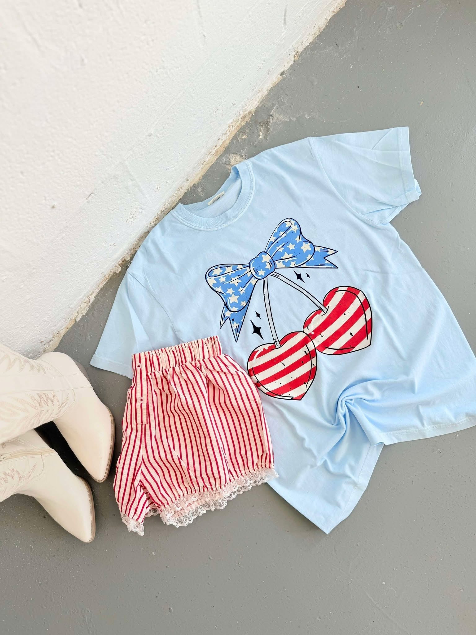 Light blue t-shirt with red and white heart cherry design and red shorts on a light gray surface.