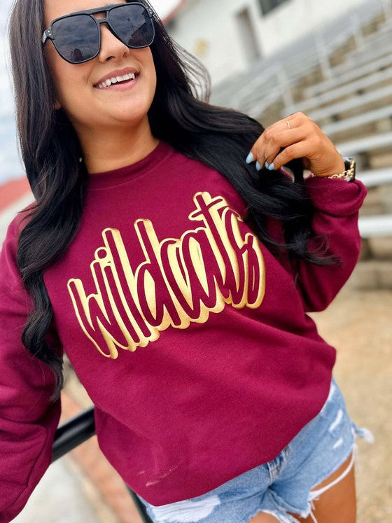 Woman wearing a maroon sweatshirt with 'Wildcats' in gold letters and denim shorts.