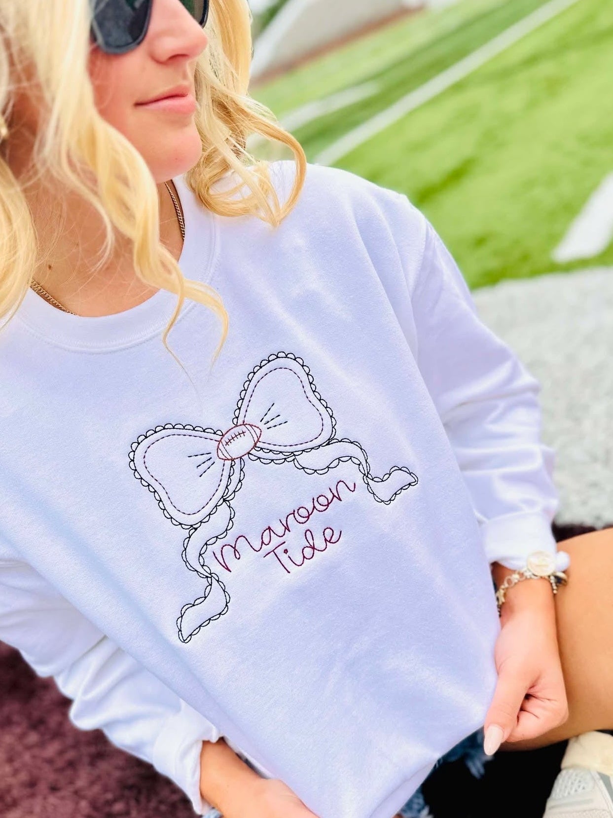 Person wearing a white sweatshirt with a bow design and 'Maroon 5' text, sitting outdoors.