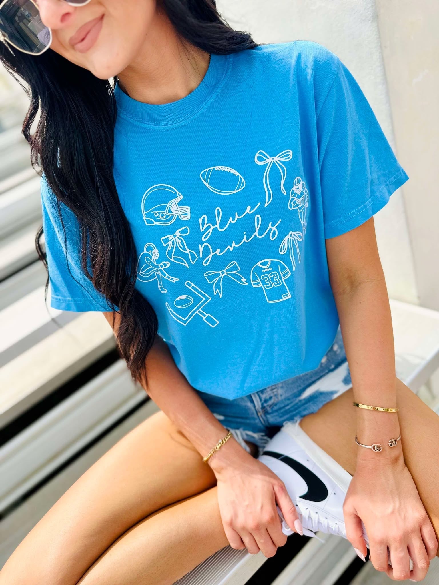 Person wearing a blue t-shirt with white graphics and text, sitting on a bench.