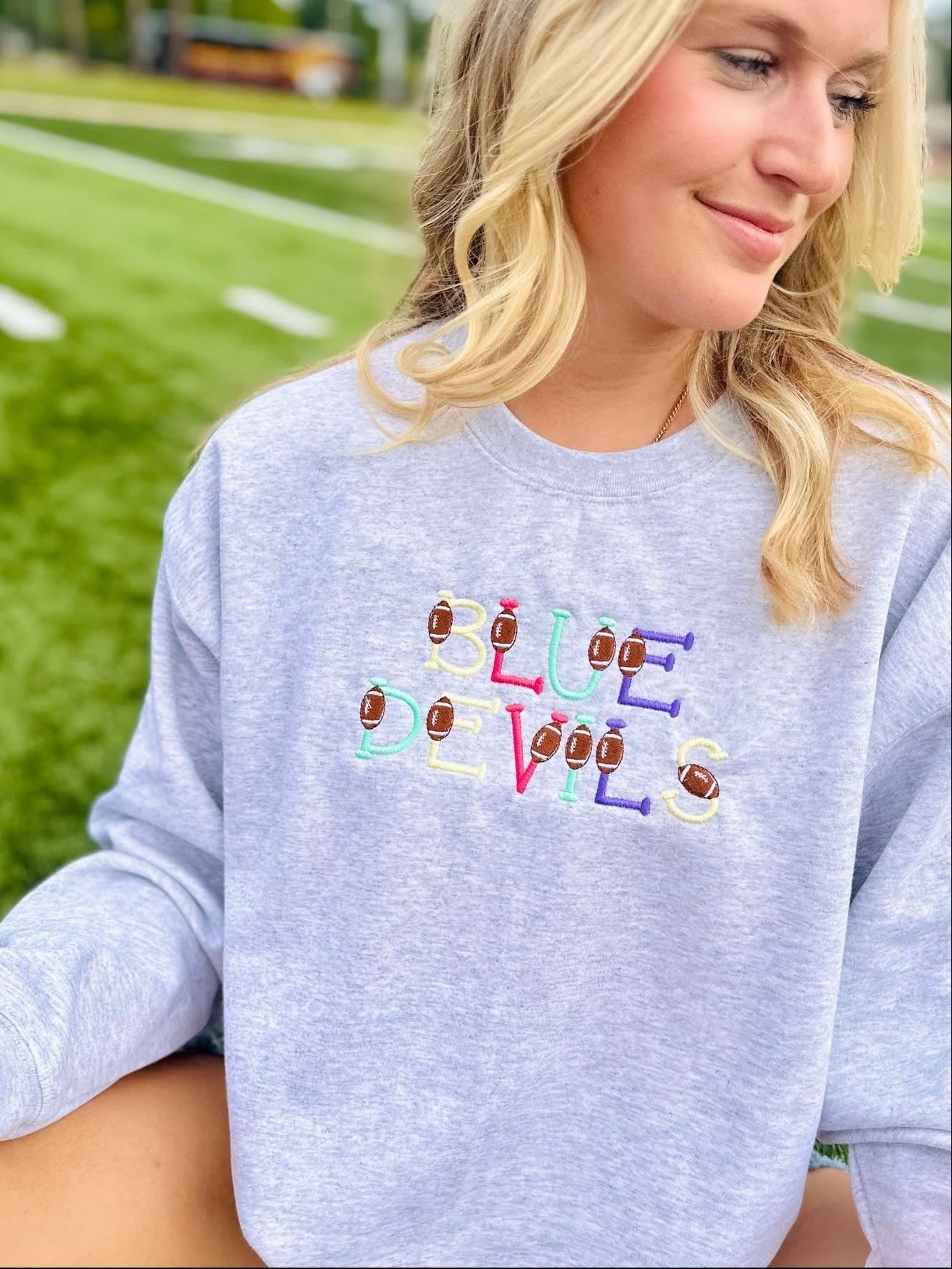 Person wearing a gray sweatshirt with 'Blue Devils' text and football icons on a sports field background