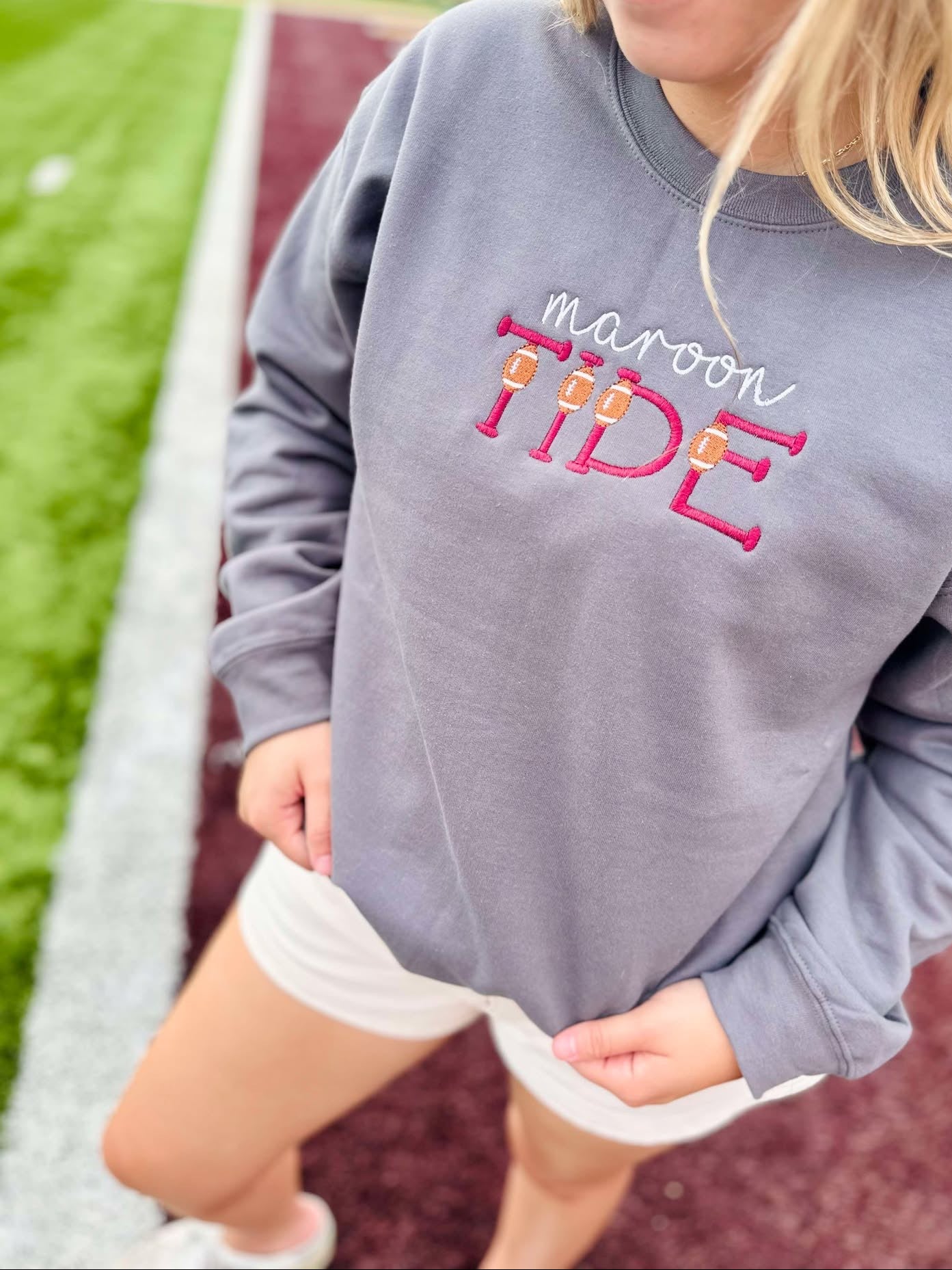 Person wearing a gray sweatshirt with 'maroon TIDE' text on a sports field background