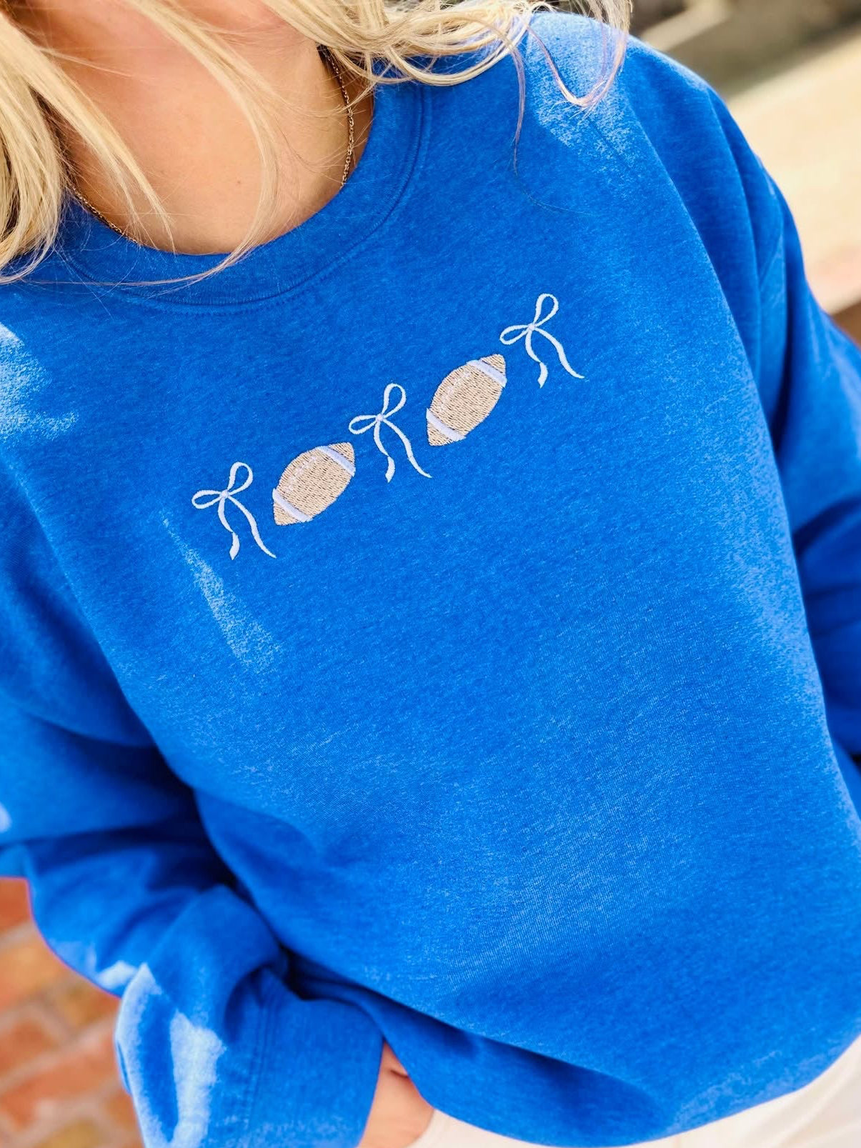 Person wearing a blue sweatshirt with white bow and football designs on a blurred background