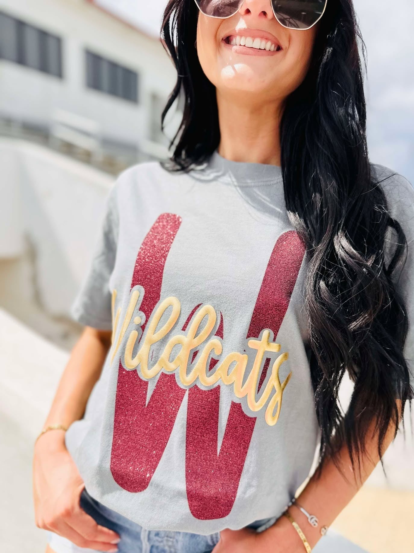 Woman wearing a gray t-shirt with 'Wildcats' printed on it, standing outdoors.