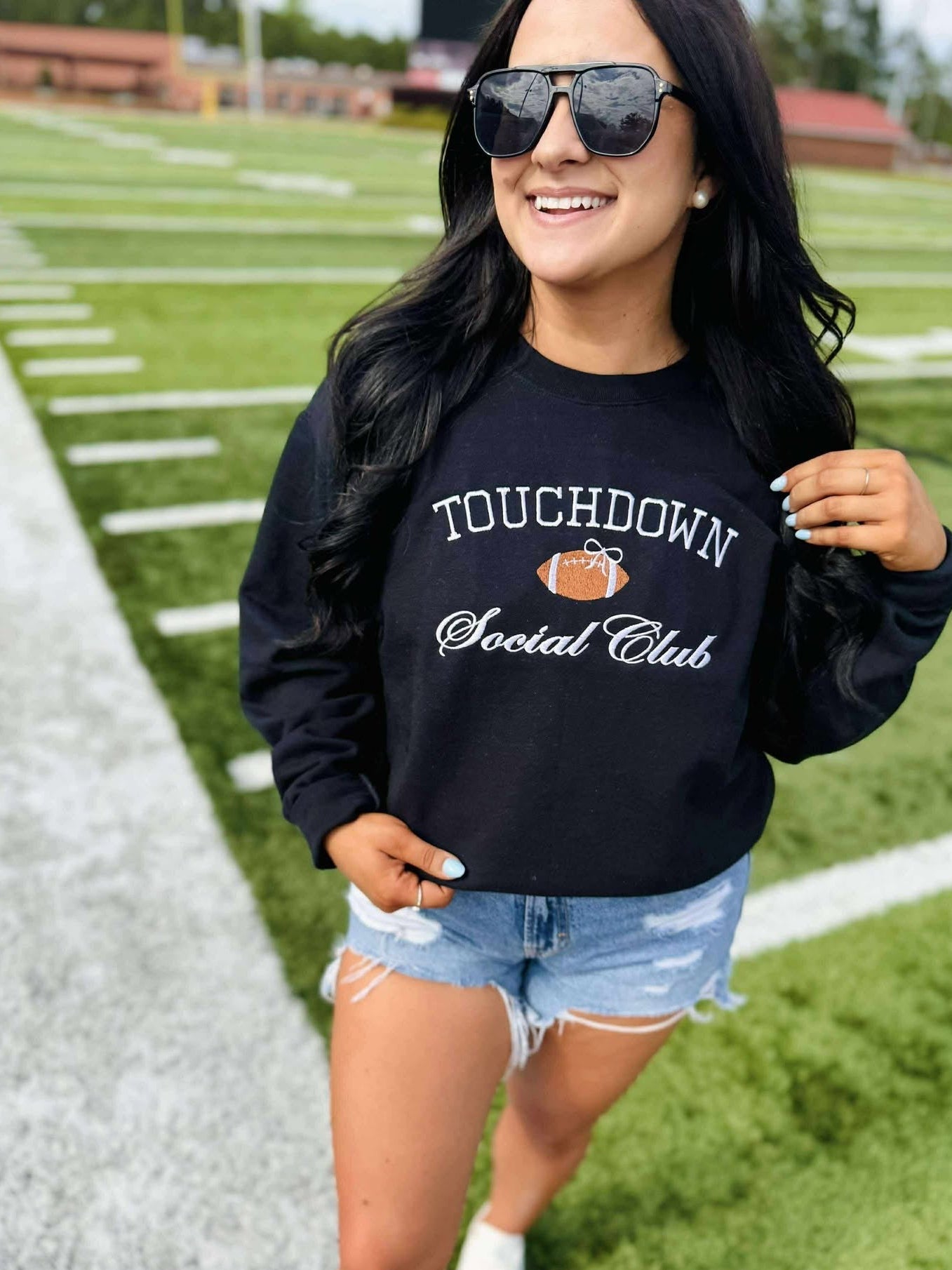 Woman wearing a black sweatshirt with 'Touchdown Social Club' text on a grassy field.