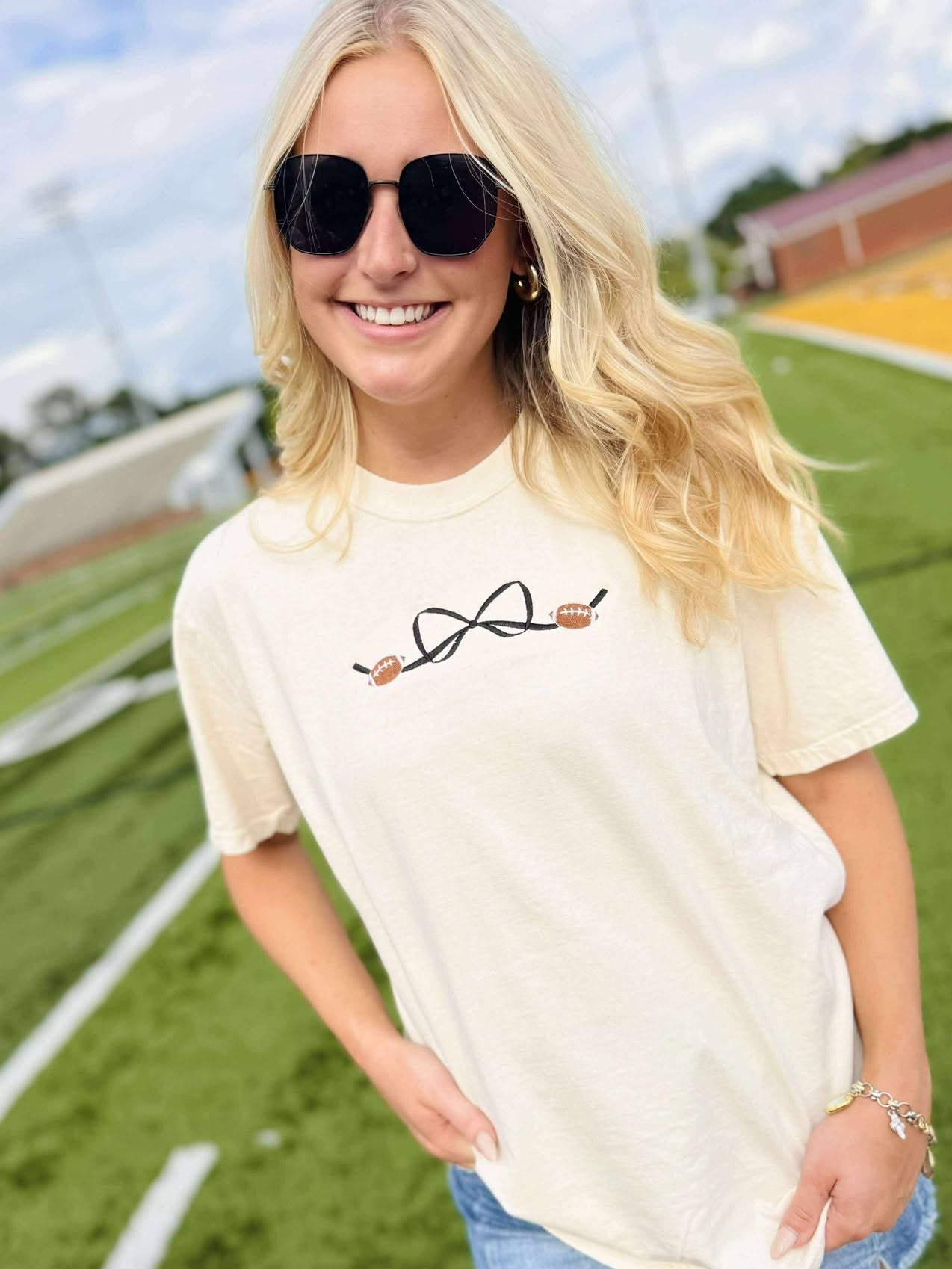Woman wearing a cream t-shirt with a bow football design on a sports field