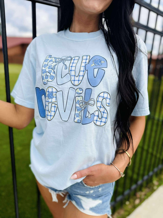 Person wearing a light blue t-shirt with 'Blue Devils' text and plaid design outdoors.