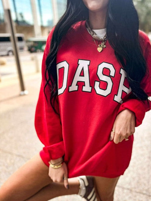 Person wearing a red sweatshirt with 'DASH'  varsity custom print on it, standing outdoors.