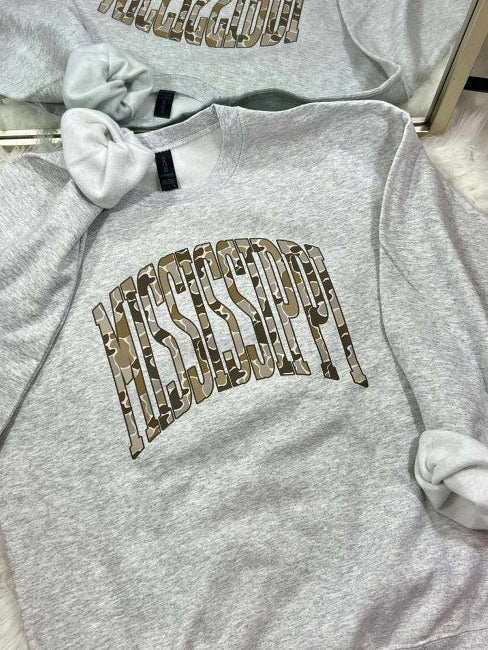Gray sweatshirt with decorative duck camo text MISSISSIPPI curved arched on a fluffy surface