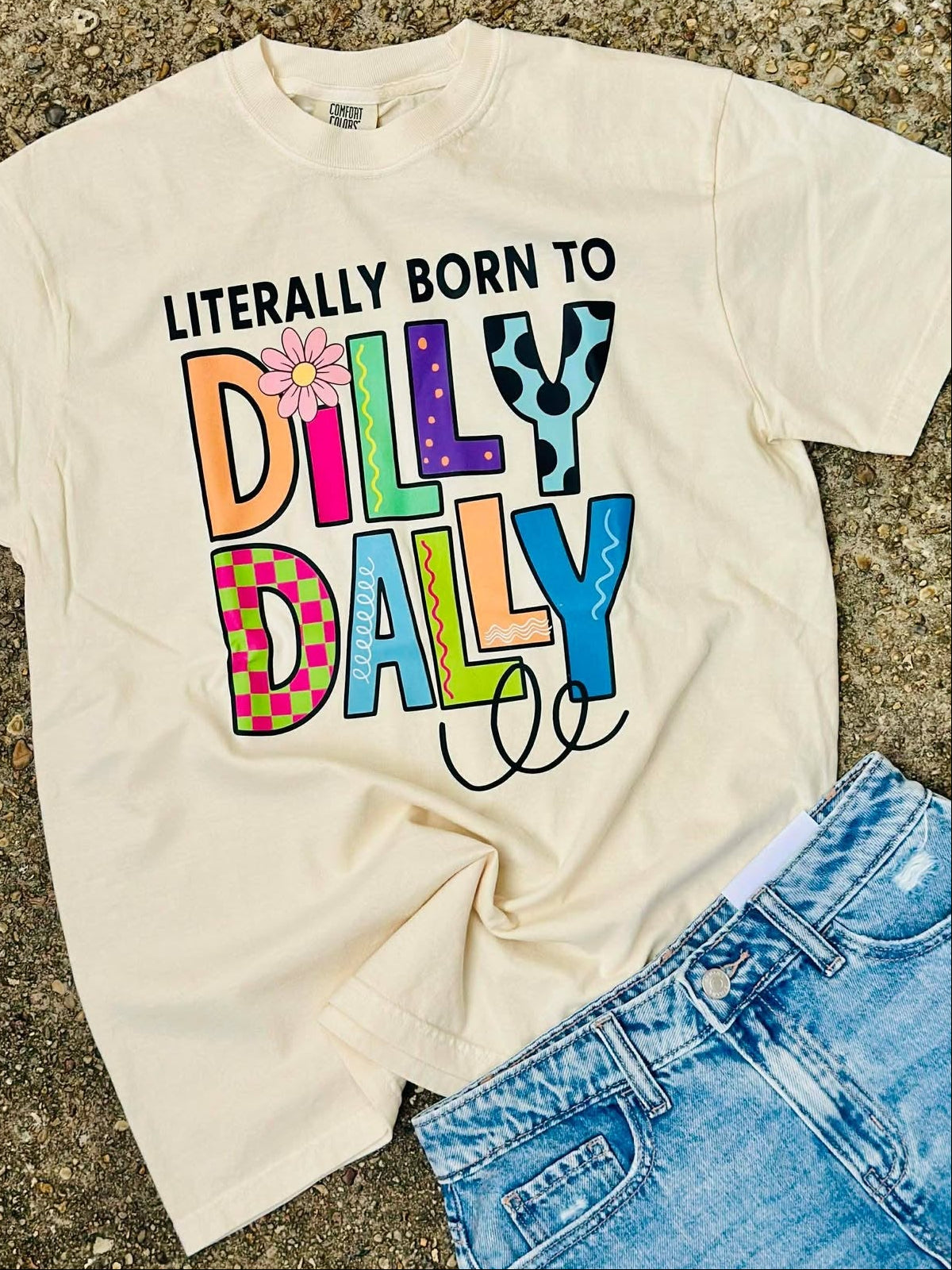 Beige t-shirt with colorful text 'Dilly Dally' on a textured surface