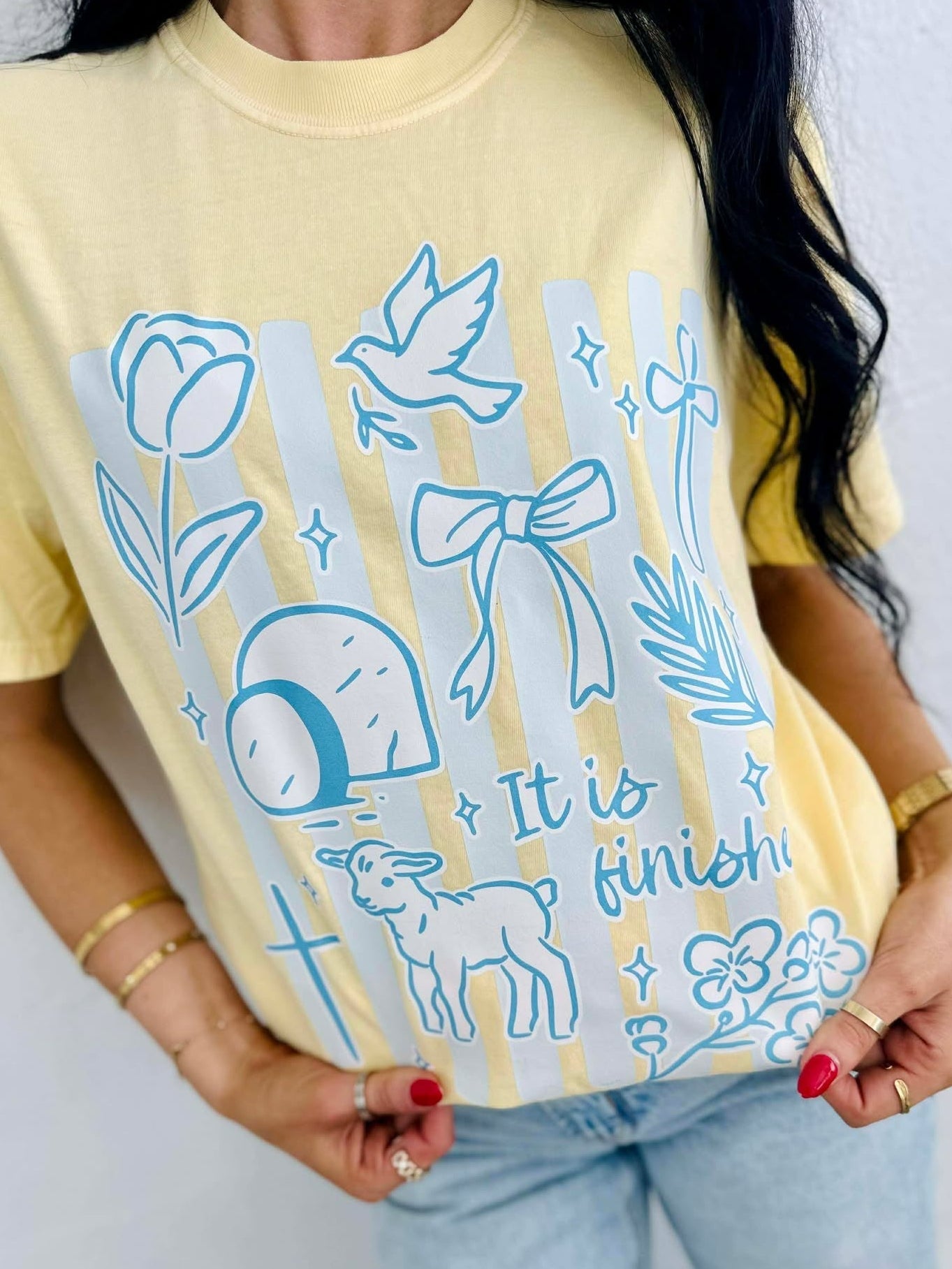 Person wearing a yellow t-shirt with blue illustrations and IT IS FINISHED text.
