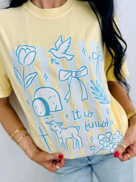 Person wearing a yellow t-shirt with blue illustrations and IT IS FINISHED text.