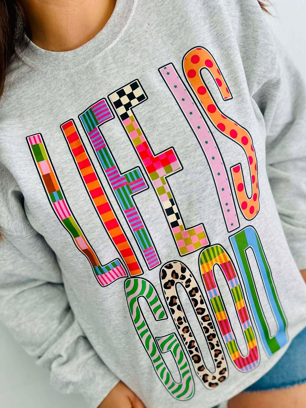 Gray sweatshirt with colorful text design worn by a person.